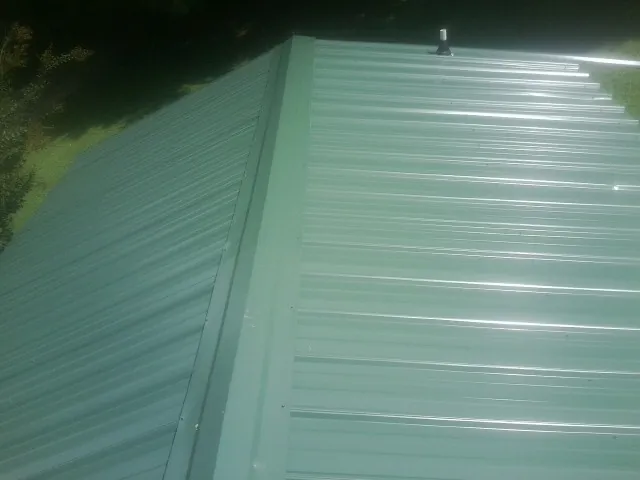 New green metal panels meeting at the ridge of a roof — Flat Roof Repair work by our crew in Circleville