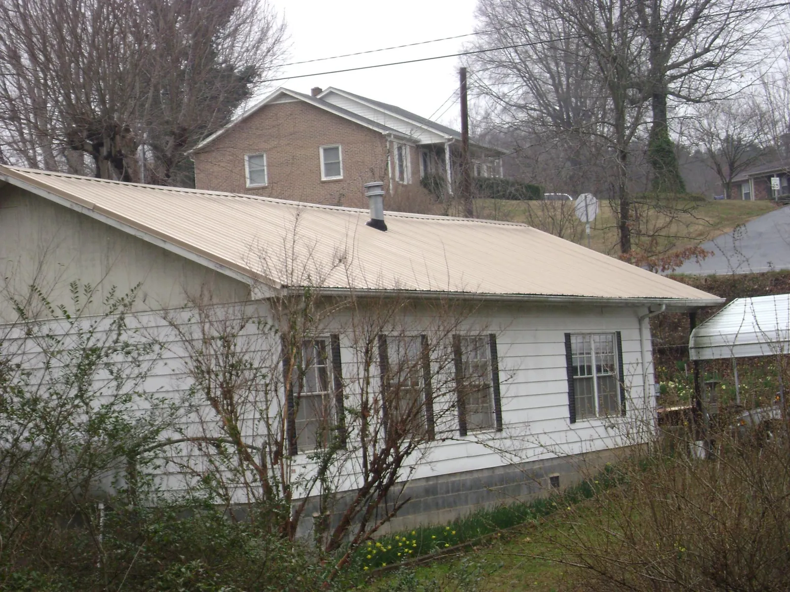 Tan metal roof on a white sided house set into a hillside — Commercial Roofing by Roofing Brothers in Circleville